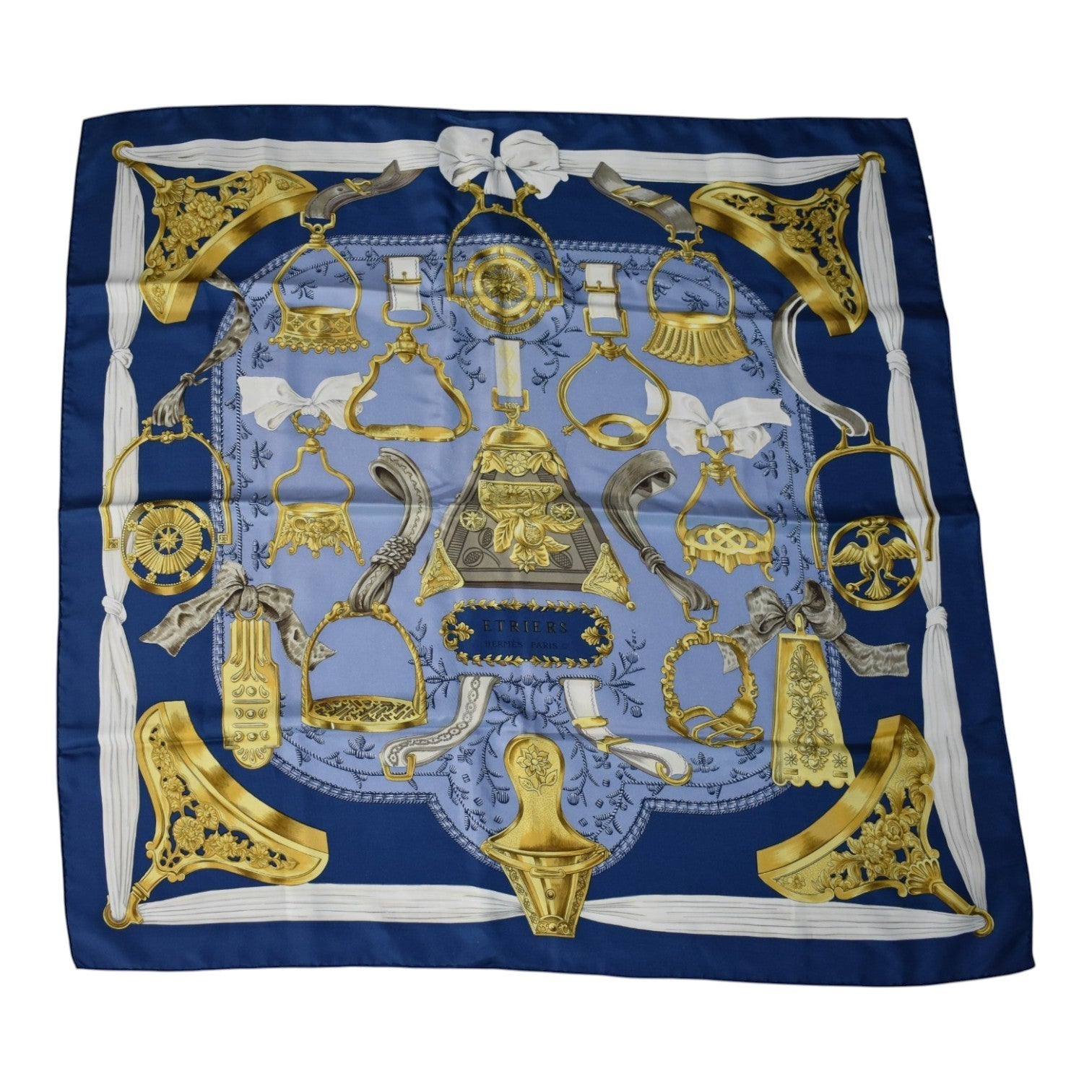 Soldi blue and gold silk scarf featuring equestrian stirrup and bridle hardware motifs. Scarf has a detailed pattern with white ribbon accents.