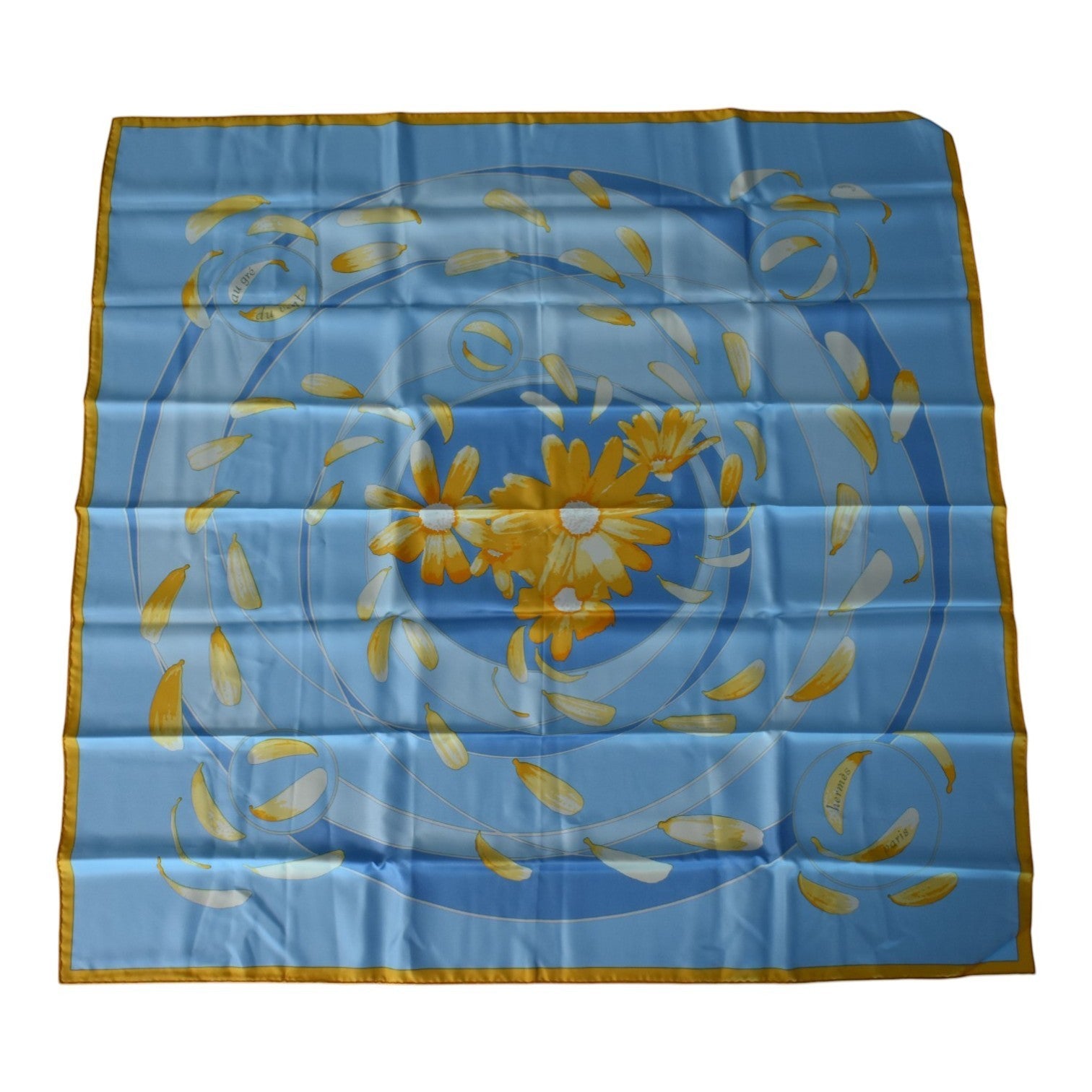 Soldi blue silk scarf with yellow flower petals and daisies. Features a swirling pattern and gold border.