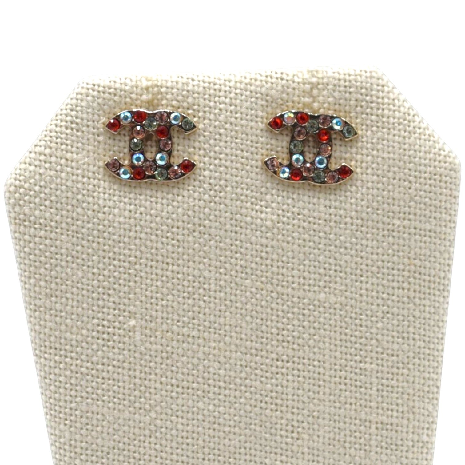 Soldi multicolor CC logo stud earrings with red, blue, and clear rhinestones on a beige display stand.